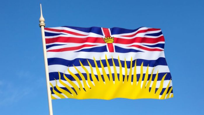 Flag of British Columbia flying in the wind against a bright blue west coast sky.