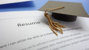 Writing a Winning Resume for New Graduates - a resume printout with a graduation cap sitting near the top.