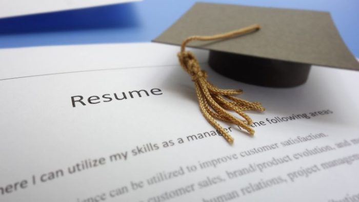Writing a Winning Resume for New Graduates - a resume printout with a graduation cap sitting near the top.