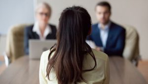 7 Common Mistakes New Graduates Make in Job Interviews - a new graduate out of school sitting in front of a panel of hiring managers during a job interview.