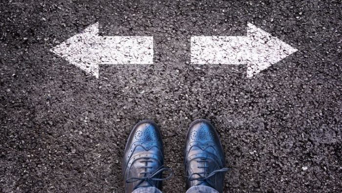 Entrepreneurship vs. Employment - a pair of feet on a road facing arrows pointing in two opposite directions.