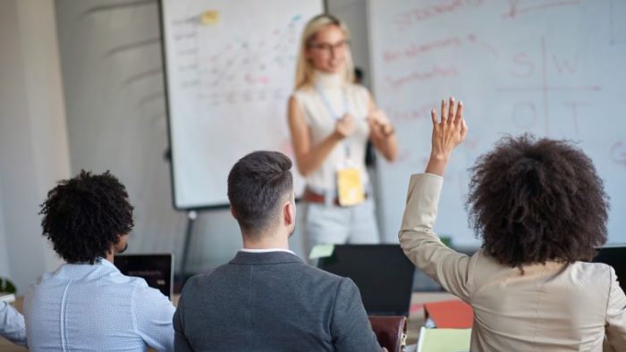 Claim Your Seat: 8 Reasons To Speak Up In The Workplace Claim Your Seat - 8 Reasons To Speak Up In The Workplace - a group of people in a work presentation with one person raising their hand.