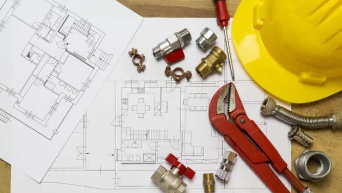 How To Write A Resume For Plumbers - large plumbing blueprint on a work table with tools and a hard hat next to it.