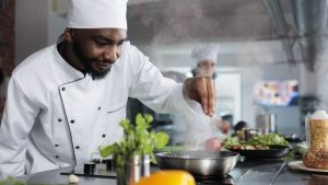 How To Write A Cook Resume - a professional cook/chef stands over a prep table creating a beautiful dish.