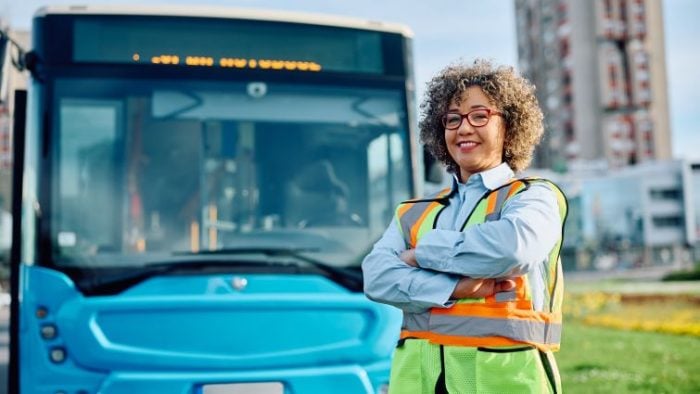 How To Write A Bus Driver Resume - a bus driver proudly stands in front of a bus.